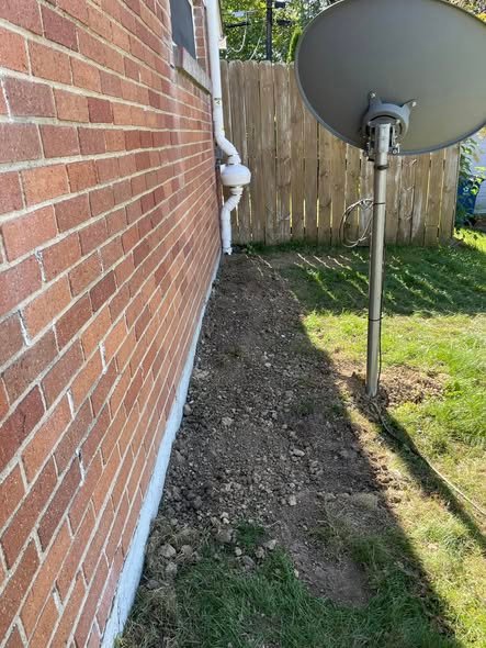 Radon system discharge pipe and trench along a backyard fence line in Johnston, IA